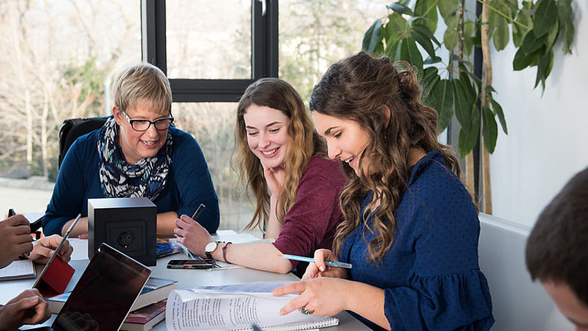 Drei Studierende sitzen in einem hellen Student Space und besprechen Lernunterlagen.