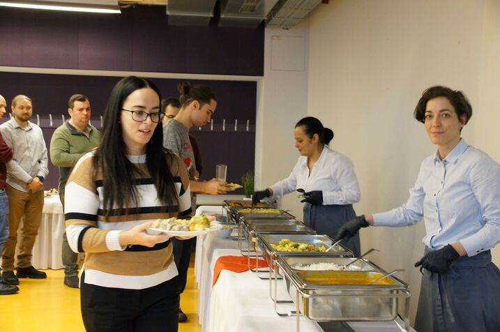 Personen stehen am Buffet und bekommen von Catering Mitarbeiter*innen Speisen gereicht.