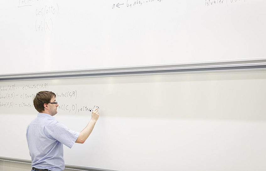 Ein Vortragender schreibt Formeln auf ein großes Whiteboard.