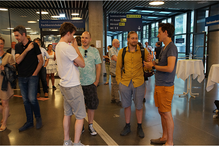 Mitarbeiter*innen der Fakultät für Informatik stehen im Foyer beisammen und unterhalten sich.